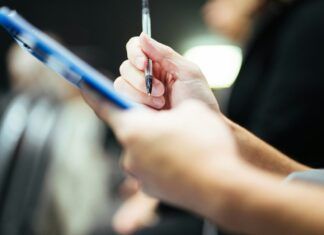Rúbricas en Educación Física Primaria: cómo evaluar por competencias con la LOMLOE Mano con bolígrafo sobre un portapapeles, símbolo de evaluación mediante rúbricas en Educación Física